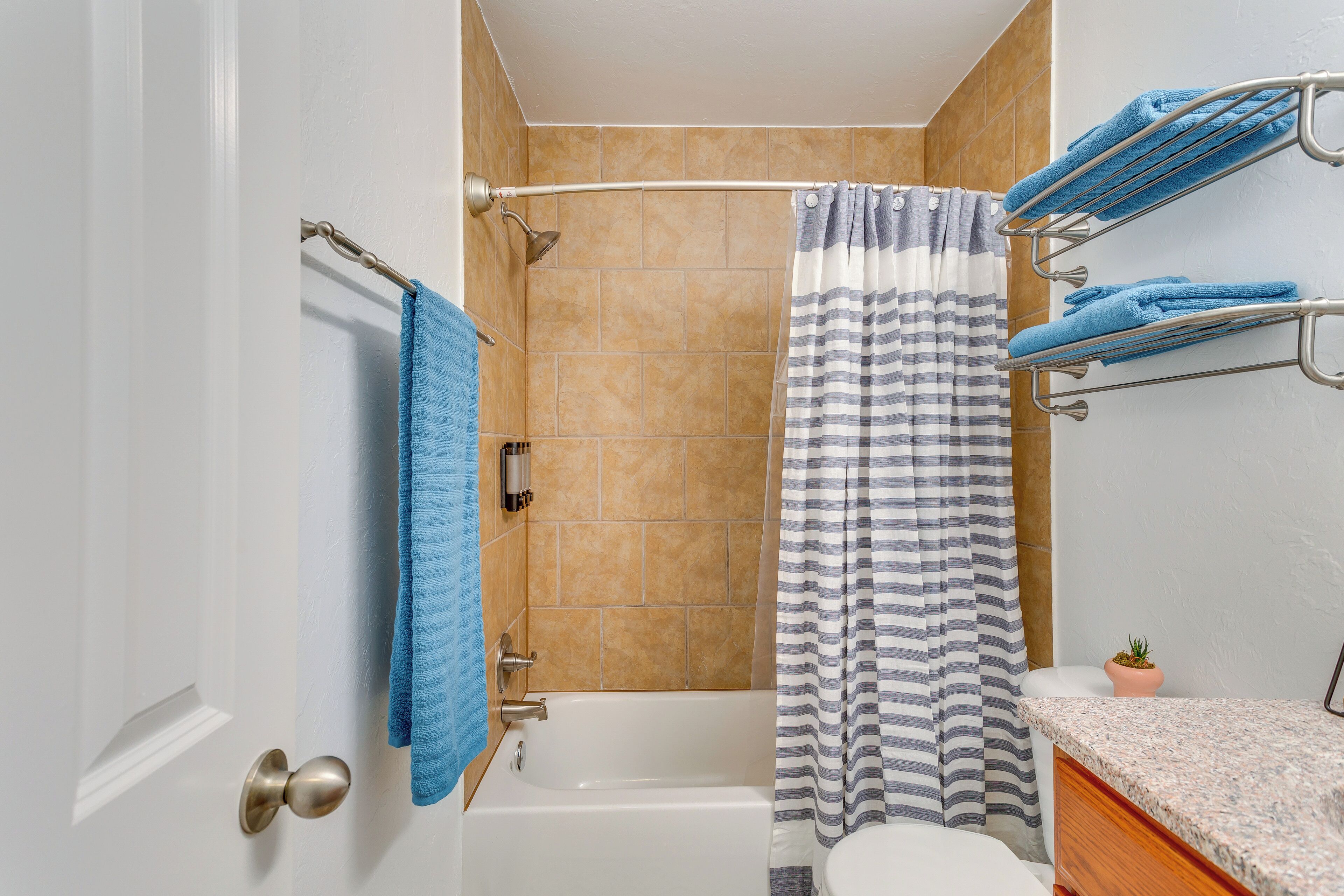 A bathroom with a bathtub, a shower curtain, a towel rack with towels, and a potted plant.