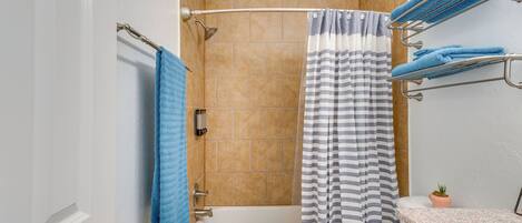A bathroom with a bathtub, a shower curtain, a towel rack with towels, and a potted plant.