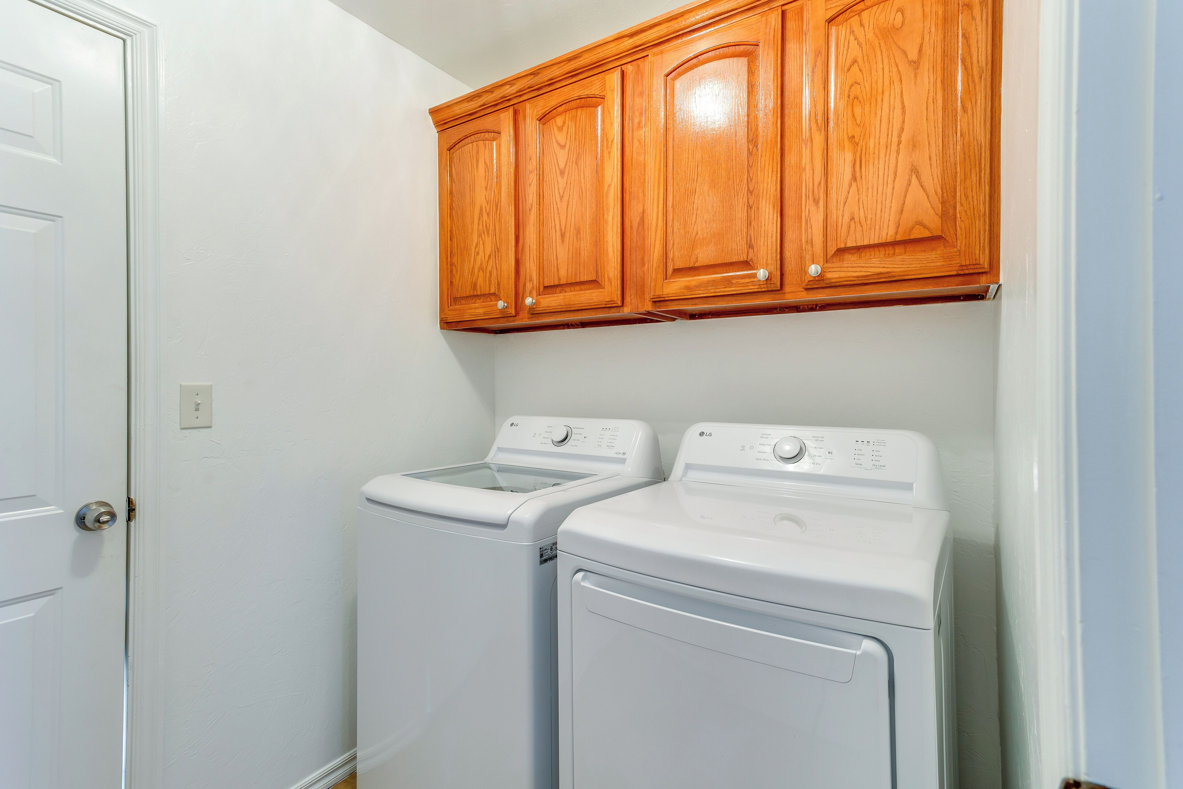 A laundry room with two white front-loading washing machines and wooden cabinets above.