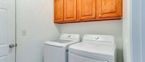 A laundry room with two white front-loading washing machines and wooden cabinets above.