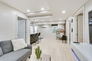 A modern living room with a grey sofa, a small table with a plant, a white console table, and a wicker chair.