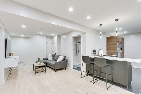 A modern kitchen with a bar area, a grey sofa, and a small table with a plant.
