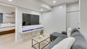 Un salon moderne avec un canapé gris, un fauteuil blanc, une table basse et un téléviseur fixé au mur.