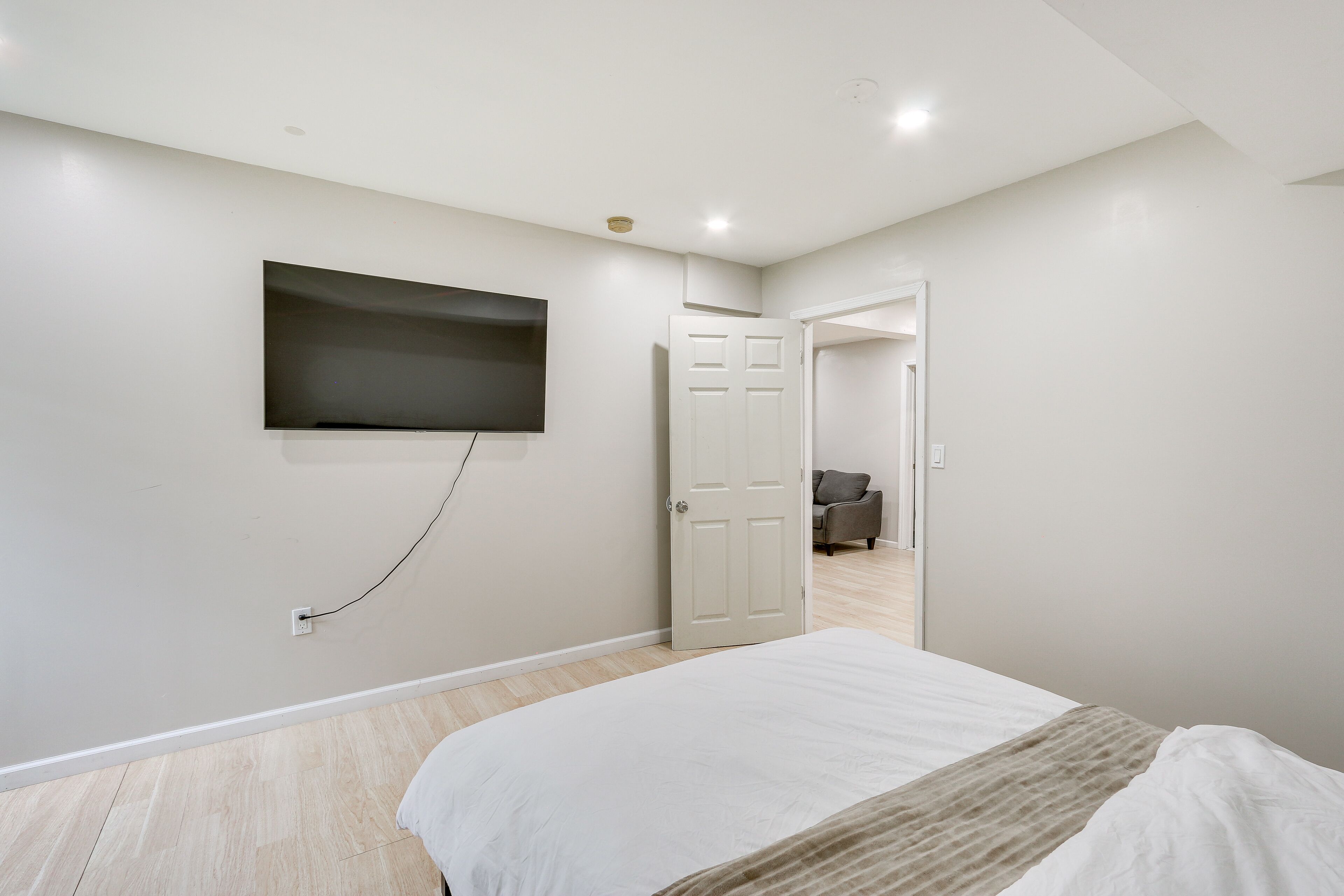 A bedroom with a bed, a TV mounted on the wall, and a door leading to another room.