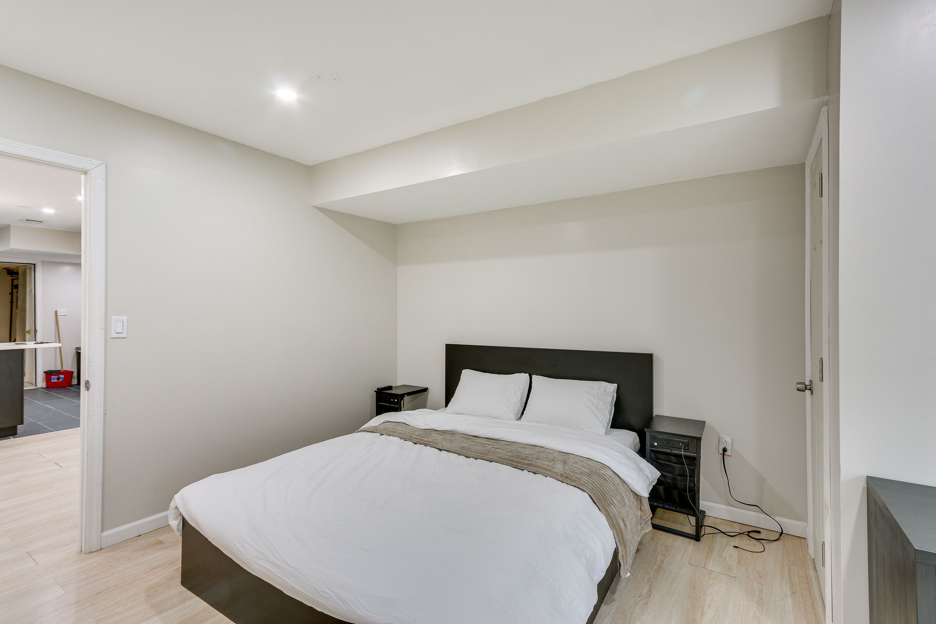 A bedroom with a large bed, a nightstand, a dresser, and a door leading to another room.