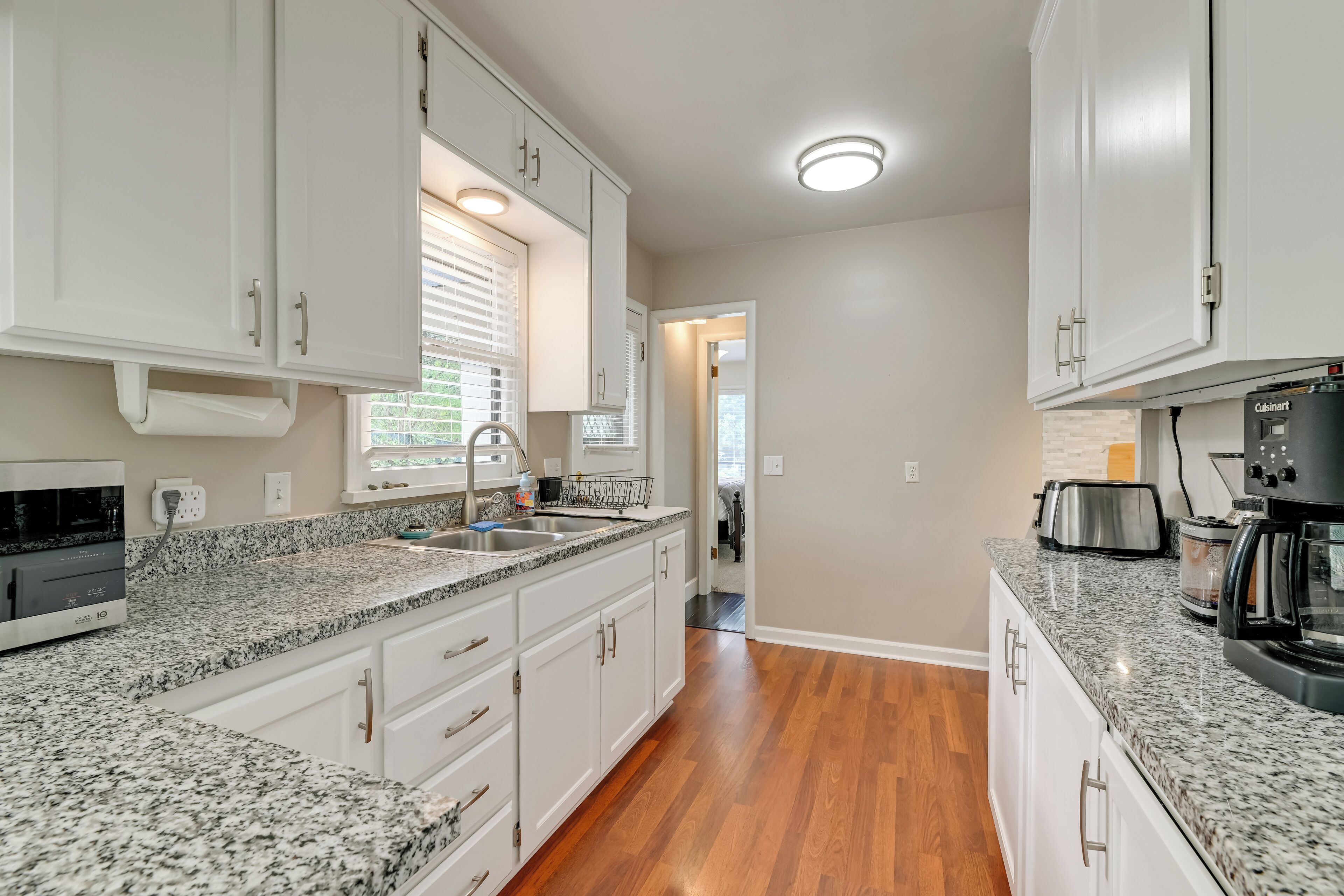 A kitchen with granite countertops, white cabinets, a built-in oven, and a coffee maker.