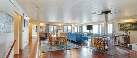 A spacious living room with a wooden floor, a blue sofa, a dining table with chairs, and a fireplace.