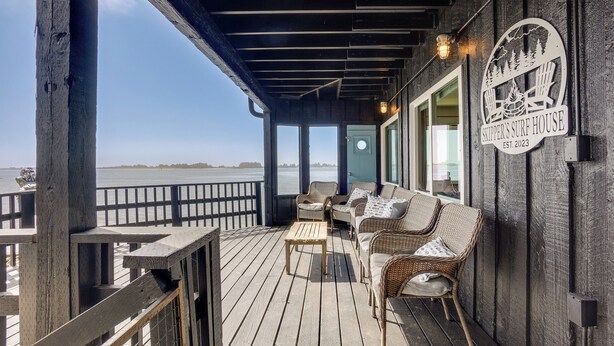 A wooden deck with wicker furniture and a view of the ocean. - Waterfront Coos Bay Retreat w/ Sauna! (Coos Bay)