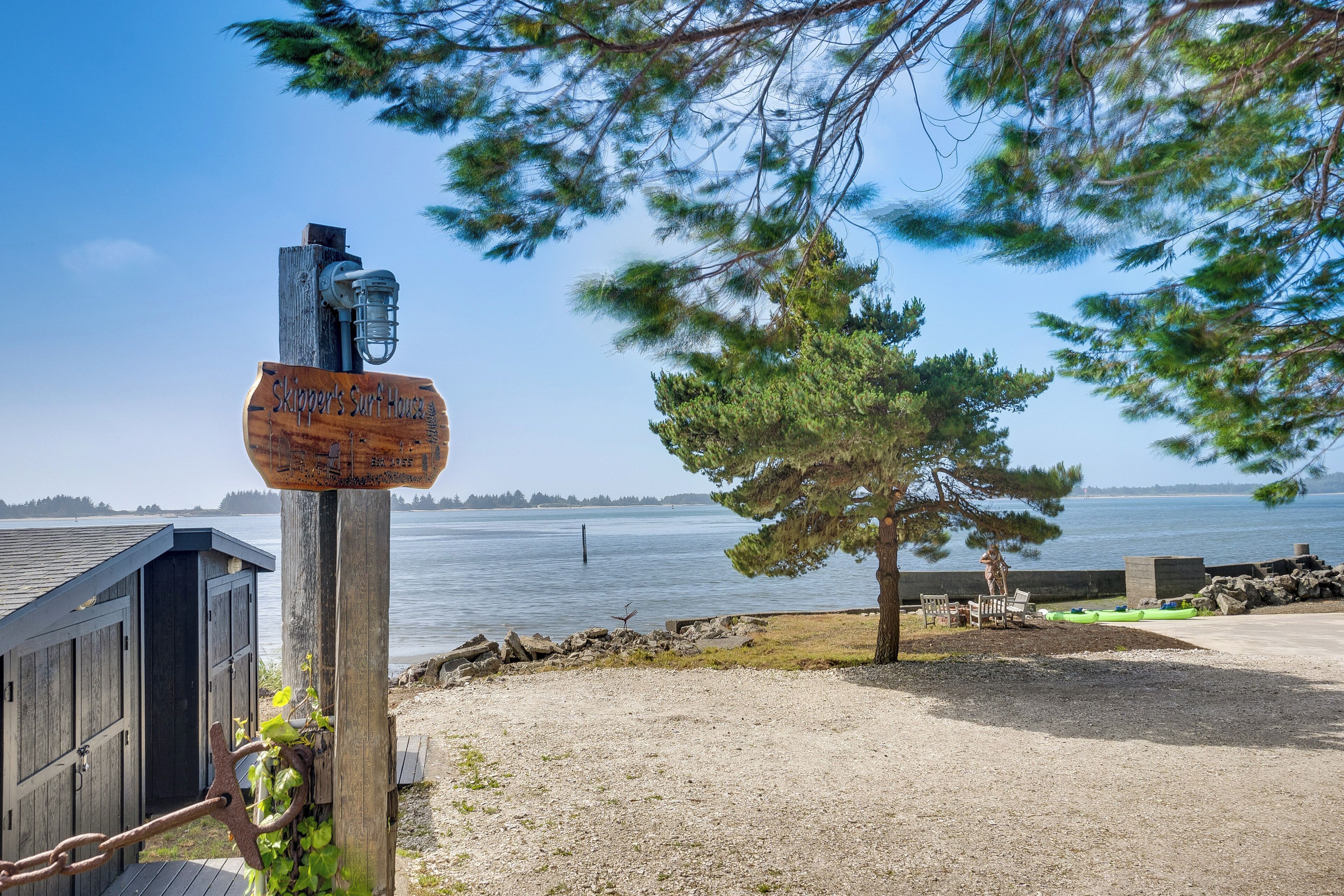 Puinen kyltti, jossa lukee ”Skipper’s Surf House”, ja näkymä rannalle, jossa on puinen rakennelma ja kajakki.