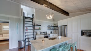 Una cocina moderna con armarios blancos, una isla central con taburetes de bar, electrodomésticos de acero inoxidable y una lámpara colgante.