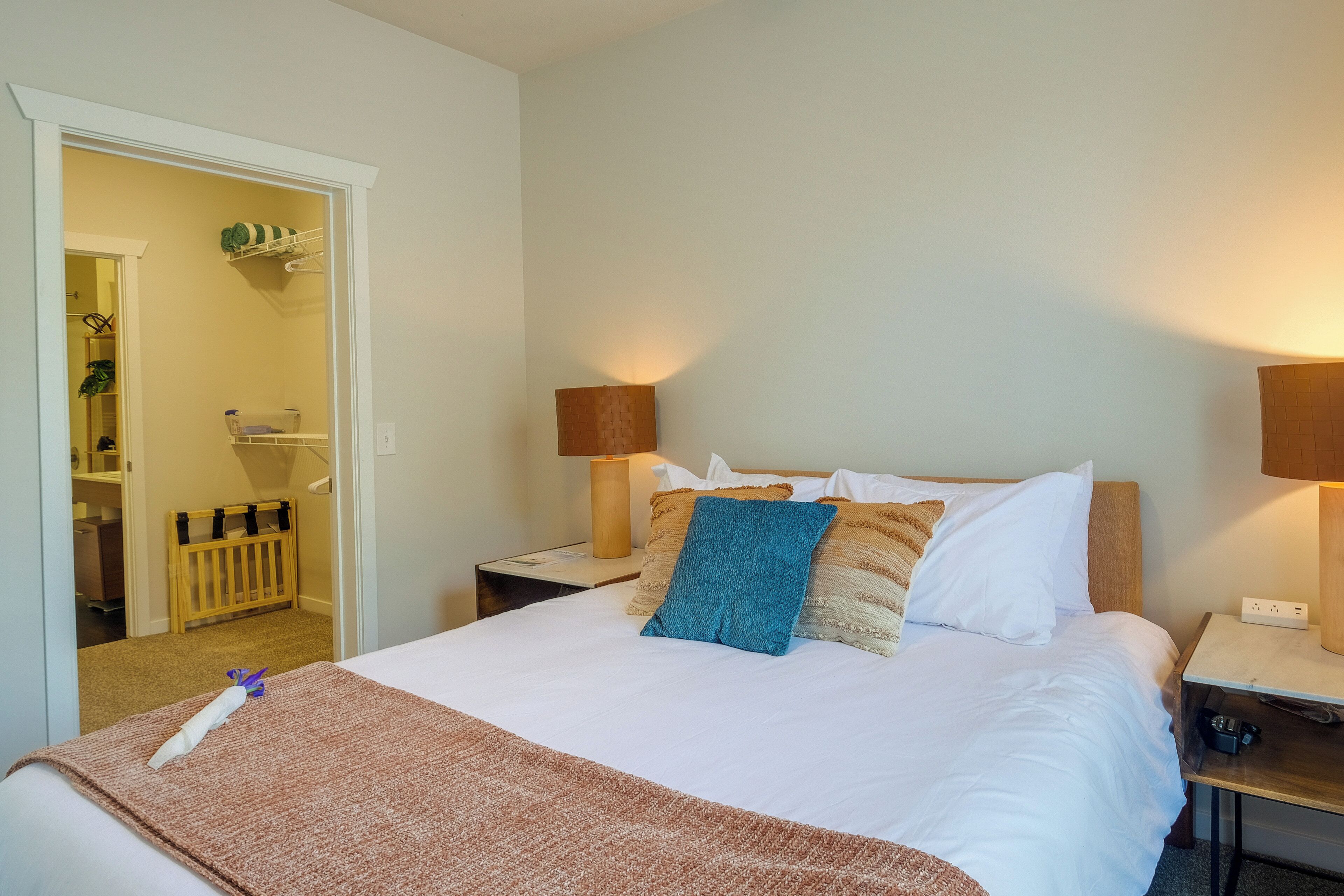 A hotel room with a bed, bedside lamps, a nightstand, a wooden crib, and a closet with shelves.