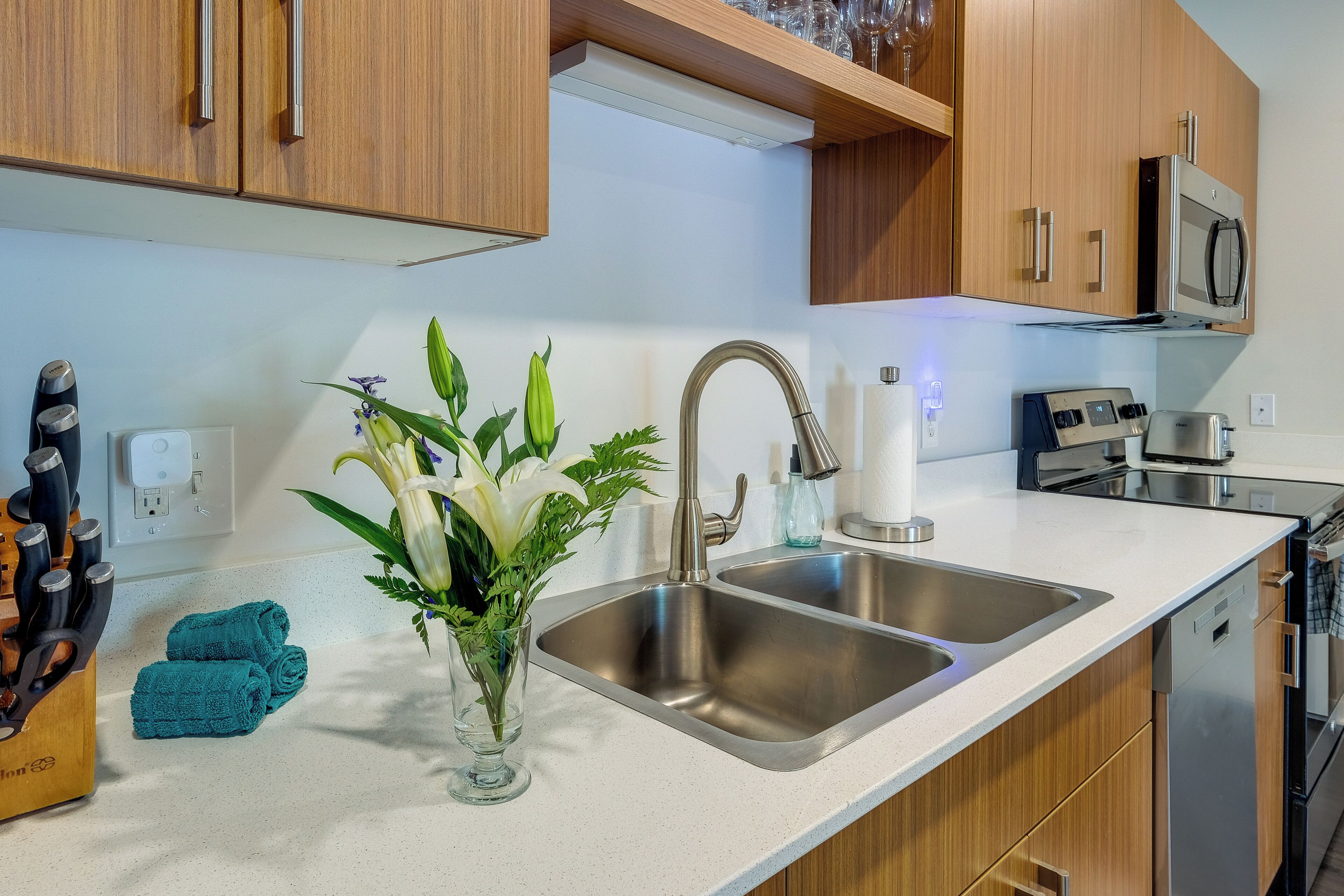 A modern kitchen with stainless steel sinks, wooden cabinets, a microwave, and a dishwasher.