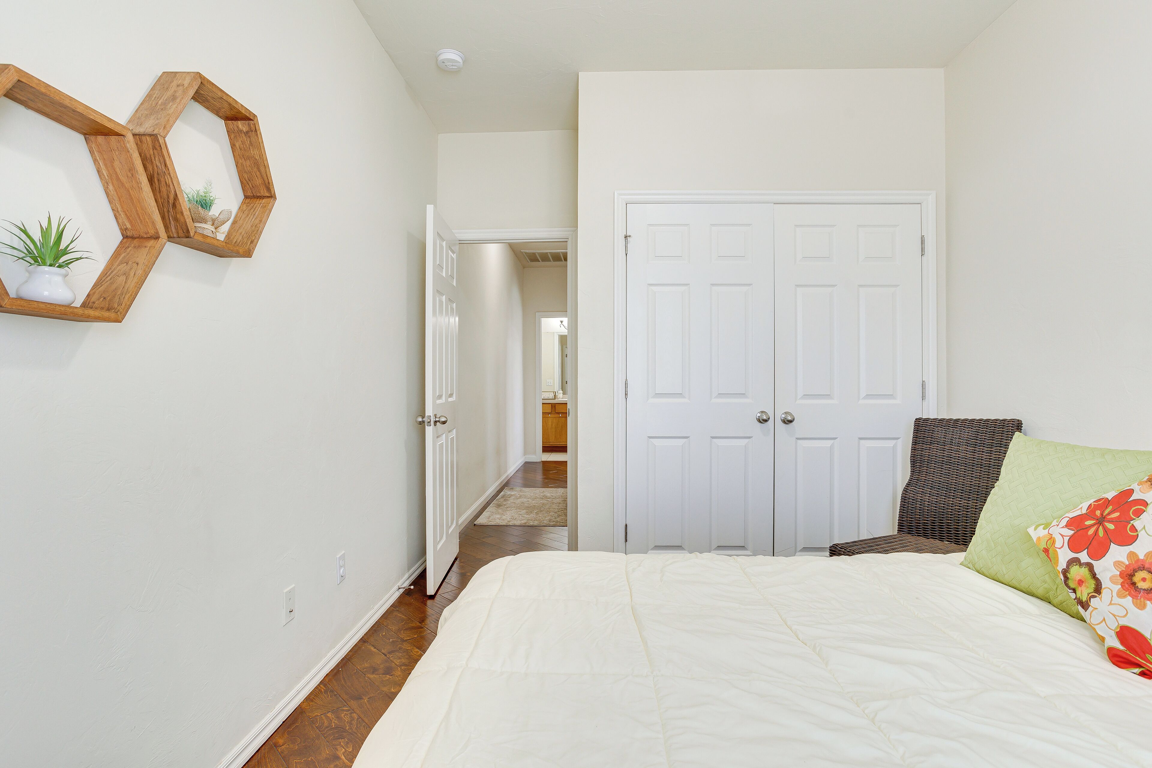 Quarto com cama, porta, cadeira e prateleira fixada na parede com uma planta.