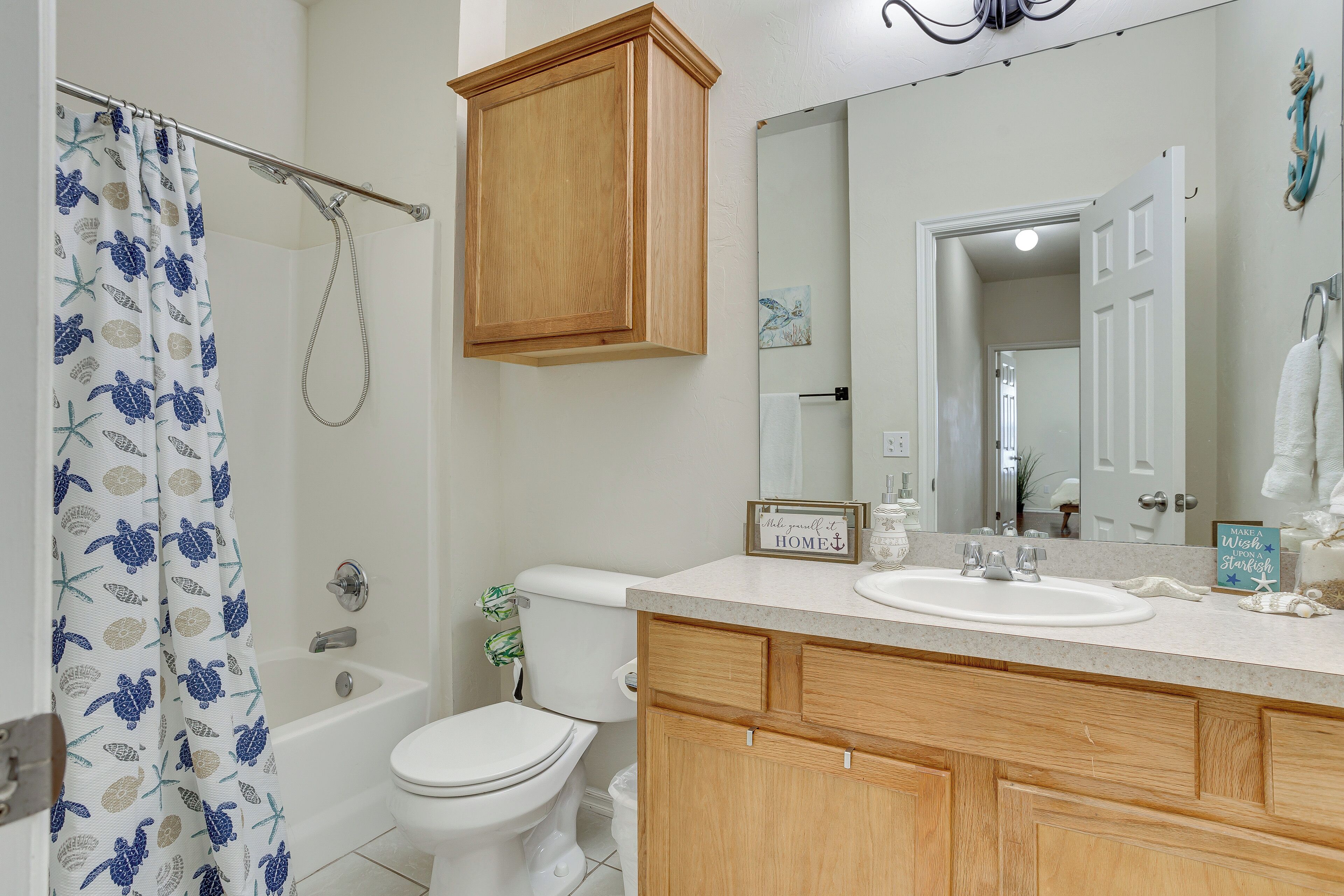 A bathroom with a shower curtain, a bathtub, a toilet, wooden cabinets, and a sink.