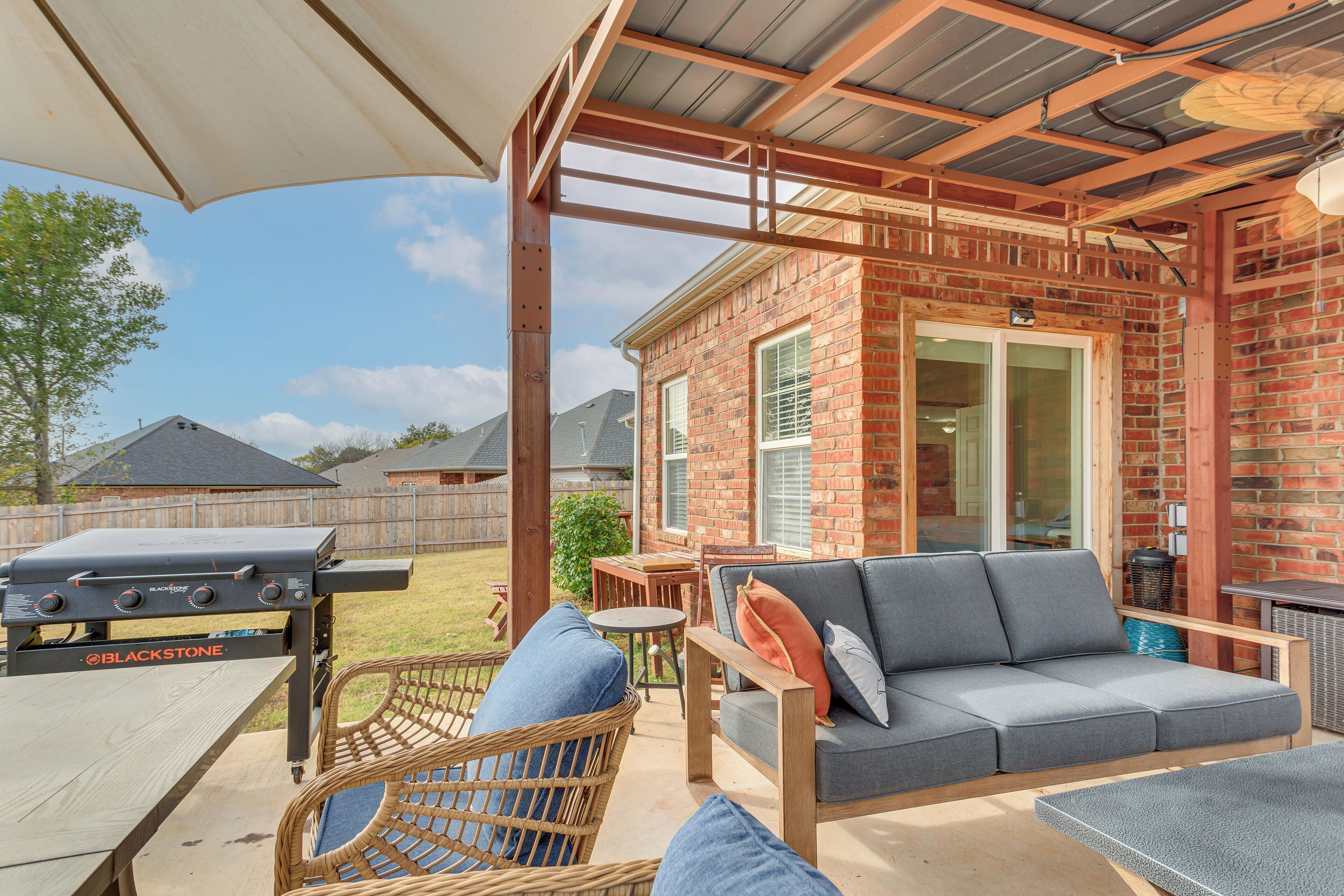 An outdoor patio with a grill, wicker furniture, and a brick house in the background.