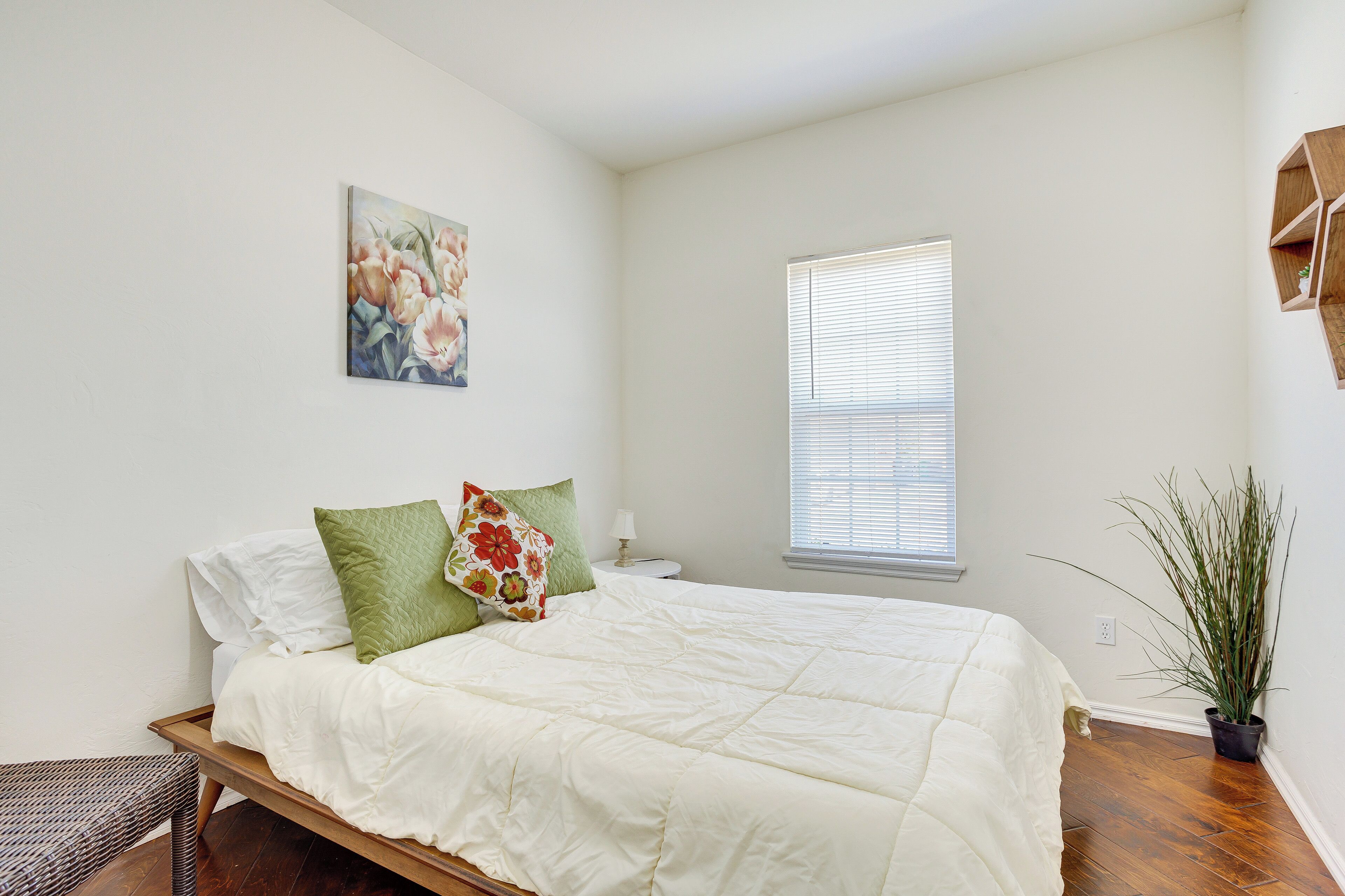 A bedroom with a bed, a nightstand, a window, and a potted plant.