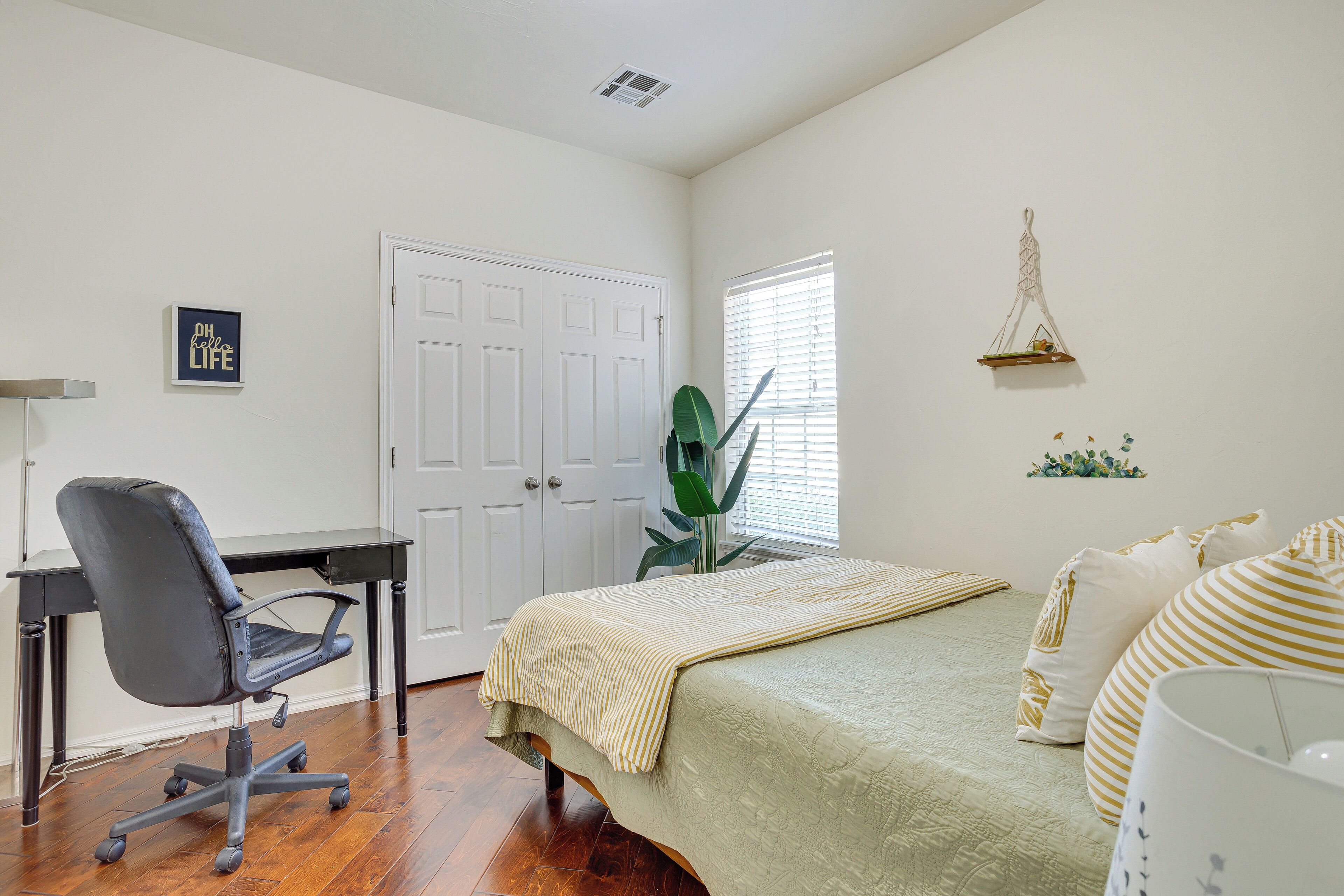 A bedroom with a bed, a desk, a chair, a window with blinds, and a wall decoration.