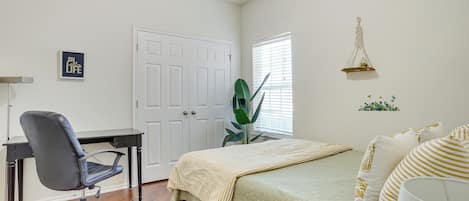 A bedroom with a bed, a desk, a chair, a window with blinds, and a wall decoration.
