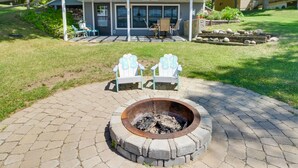 A fire pit with two Adirondack chairs, a patio area, and a house with a covered deck in the background.