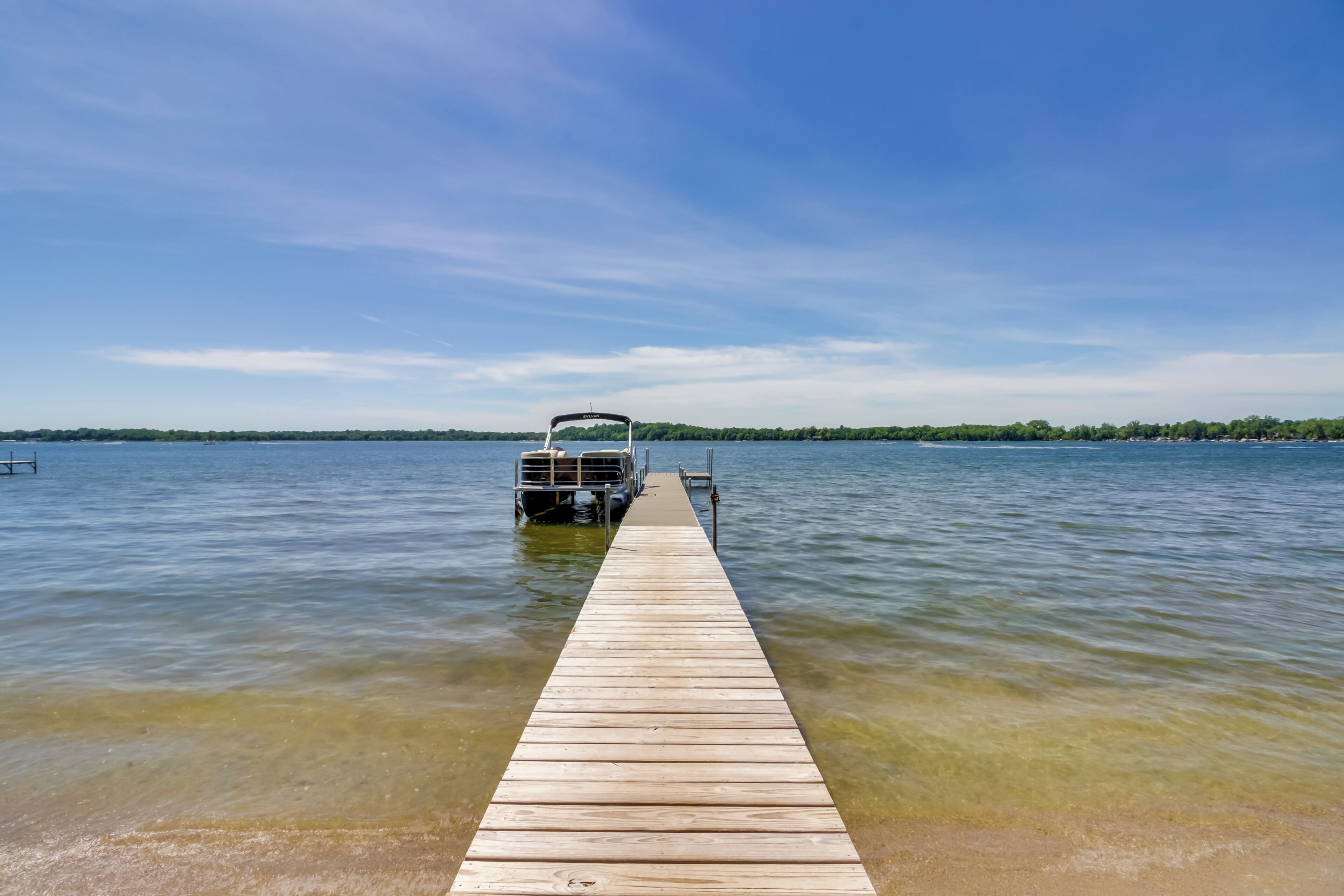 A wooden dock extending into a calm lake with a clear sky.
