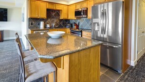 Una cocina moderna con armarios de madera, encimeras de granito, electrodomésticos de acero inoxidable y una isla grande con taburetes de bar.