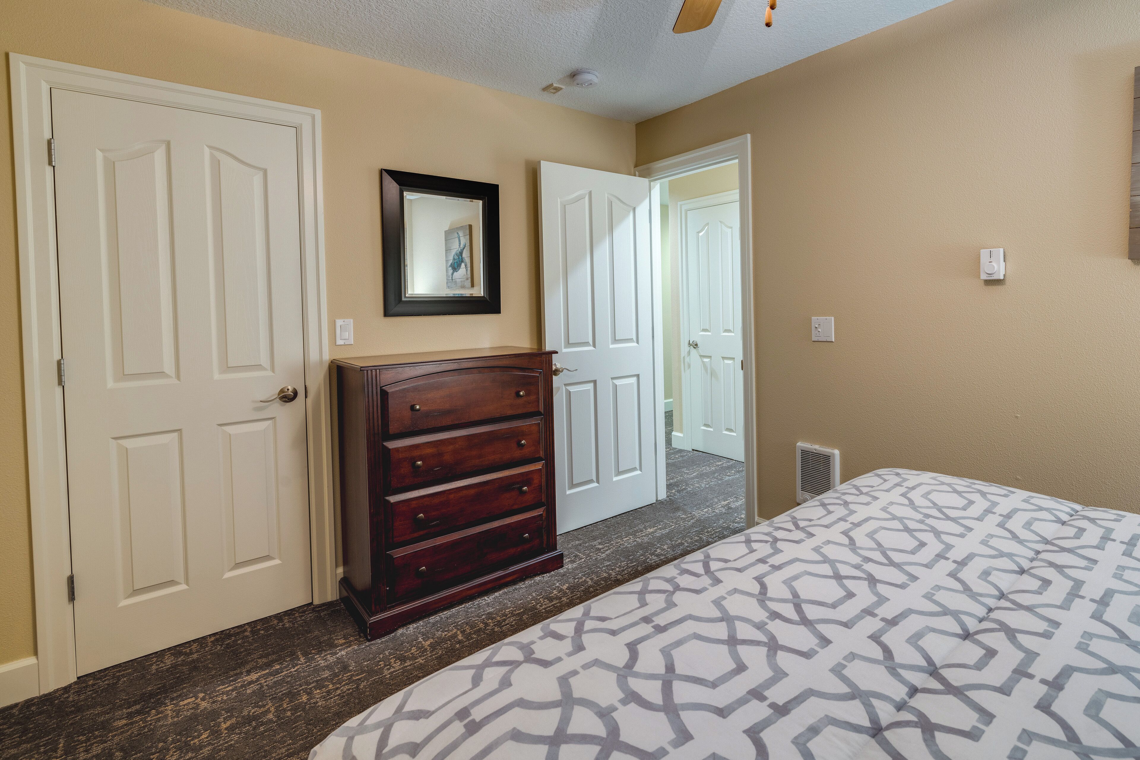 A bedroom with a patterned bedspread, a wooden dresser, and a framed picture on the wall.