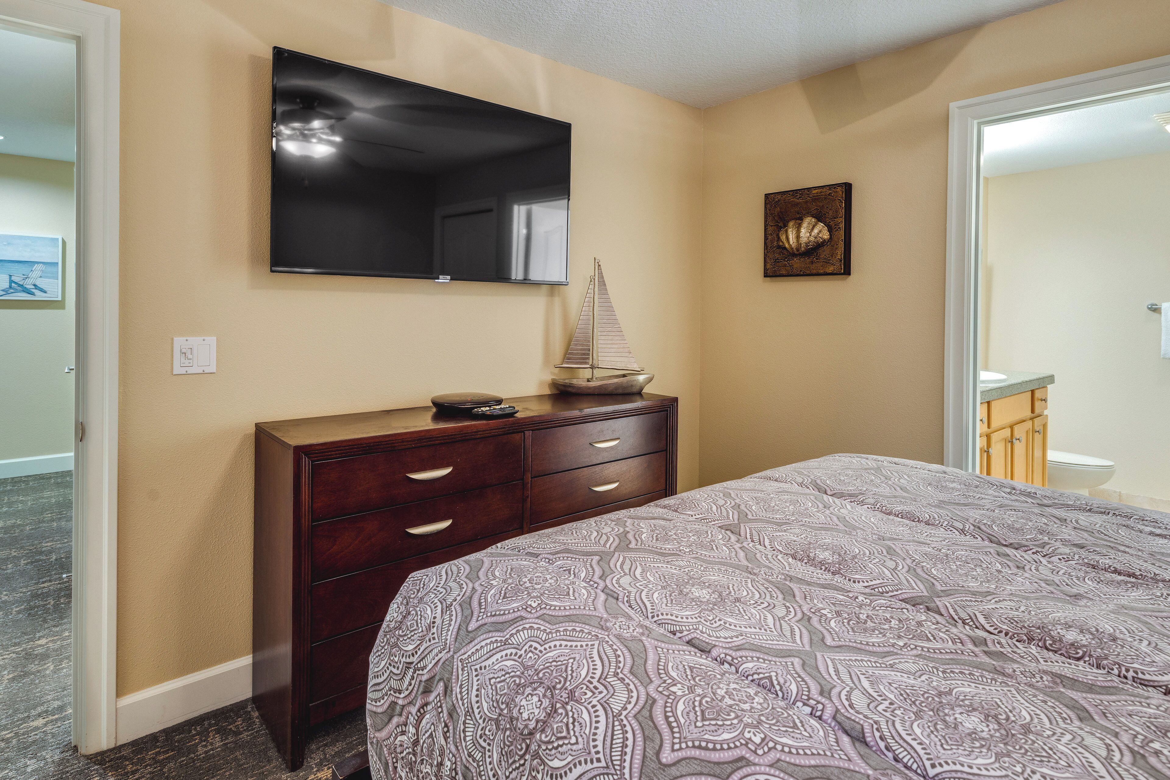 Une chambre à coucher comprenant un lit, une commode, un téléviseur fixé au mur et un tableau encadré.