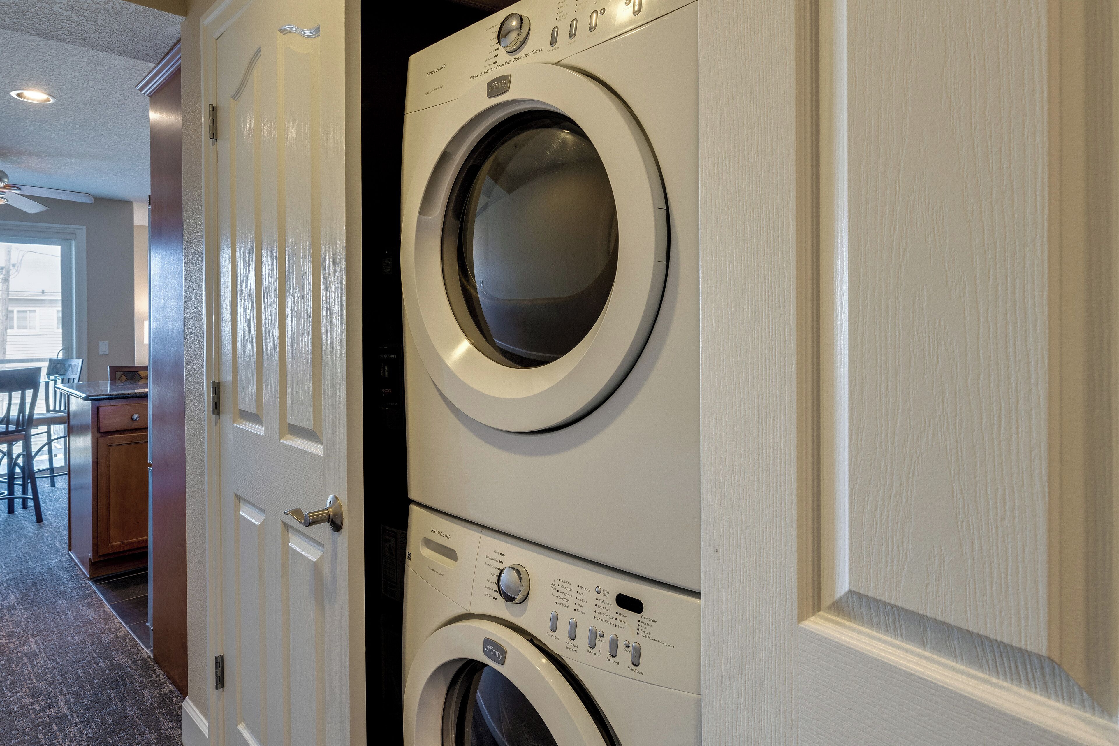 A laundry room with stacked washers and dryers, a door, and a hallway leading to a dining area.