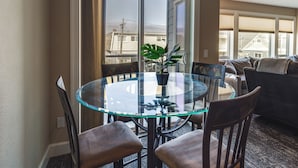 Mesa de vidrio con cuatro sillas, una planta en maceta y vistas a edificios a través de un ventanal corredero.