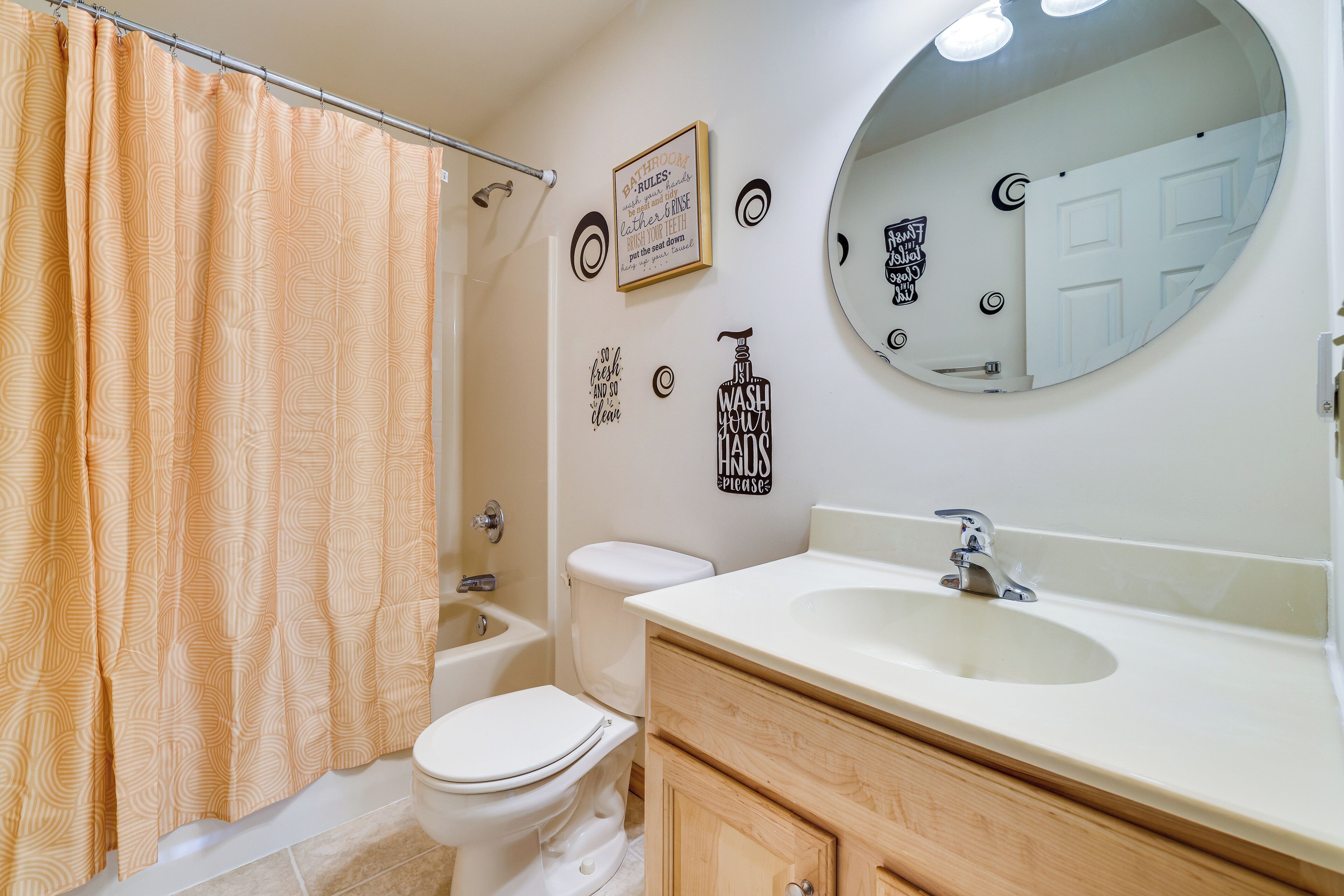 A bathroom with a shower curtain, toilet, sink, vanity, and a mirror.