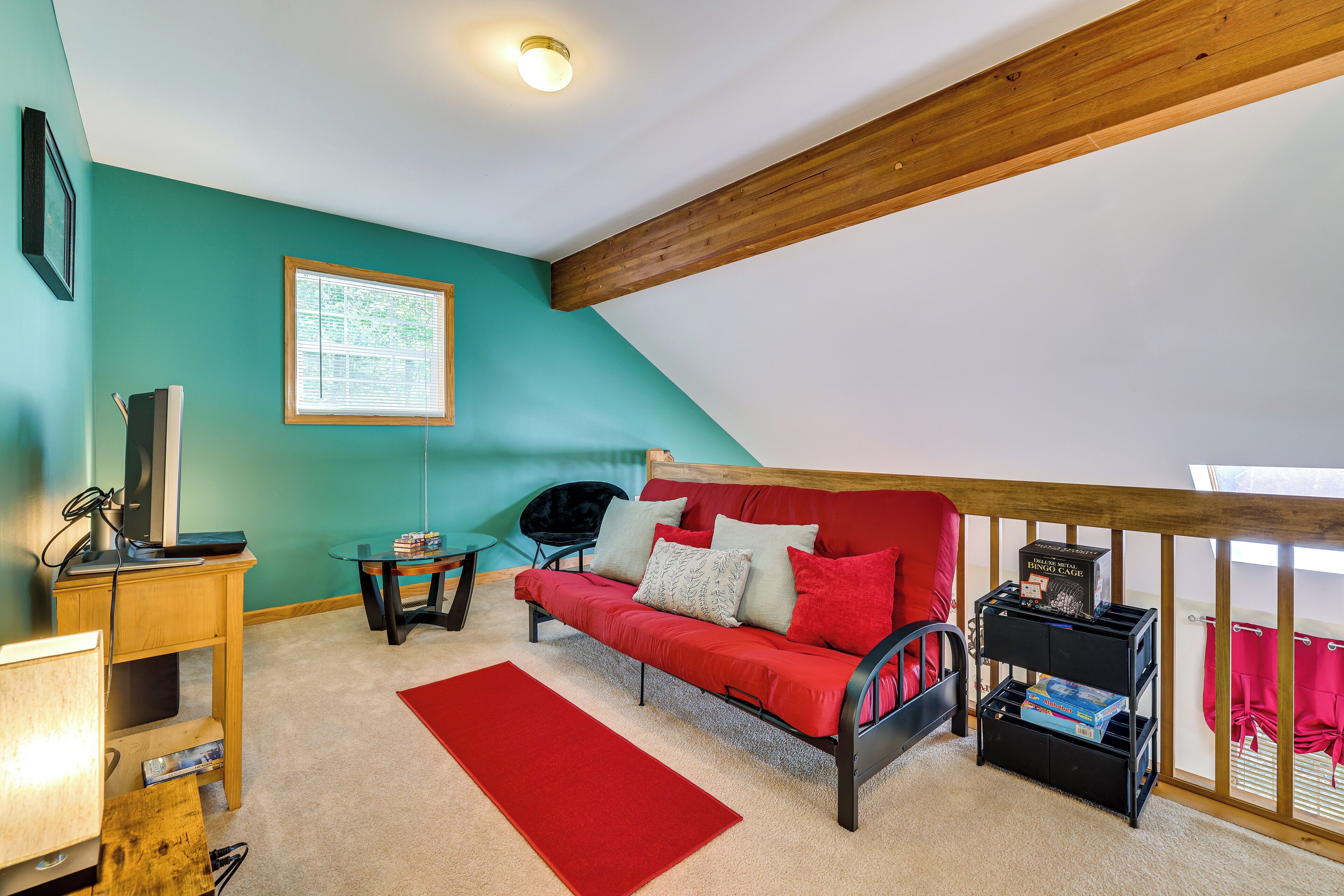 A cozy room with a red sofa, a small table, a TV, and a window with blinds.