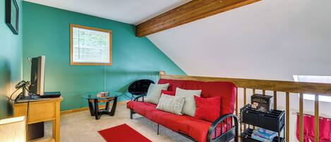 A cozy room with a red sofa, a small table, a TV, and a window with blinds.