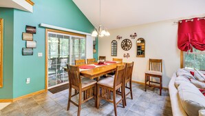 A dining area with a wooden table and chairs, a chandelier, and a red curtain. - Deck & Screened Porch: Pocono Lake Vacation Rental (Pocono Lake)