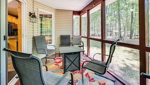 A covered porch with four chairs and a table, a wooden ceiling, and a view of a forest. - Deck & Screened Porch: Pocono Lake Vacation Rental (Pocono Lake)