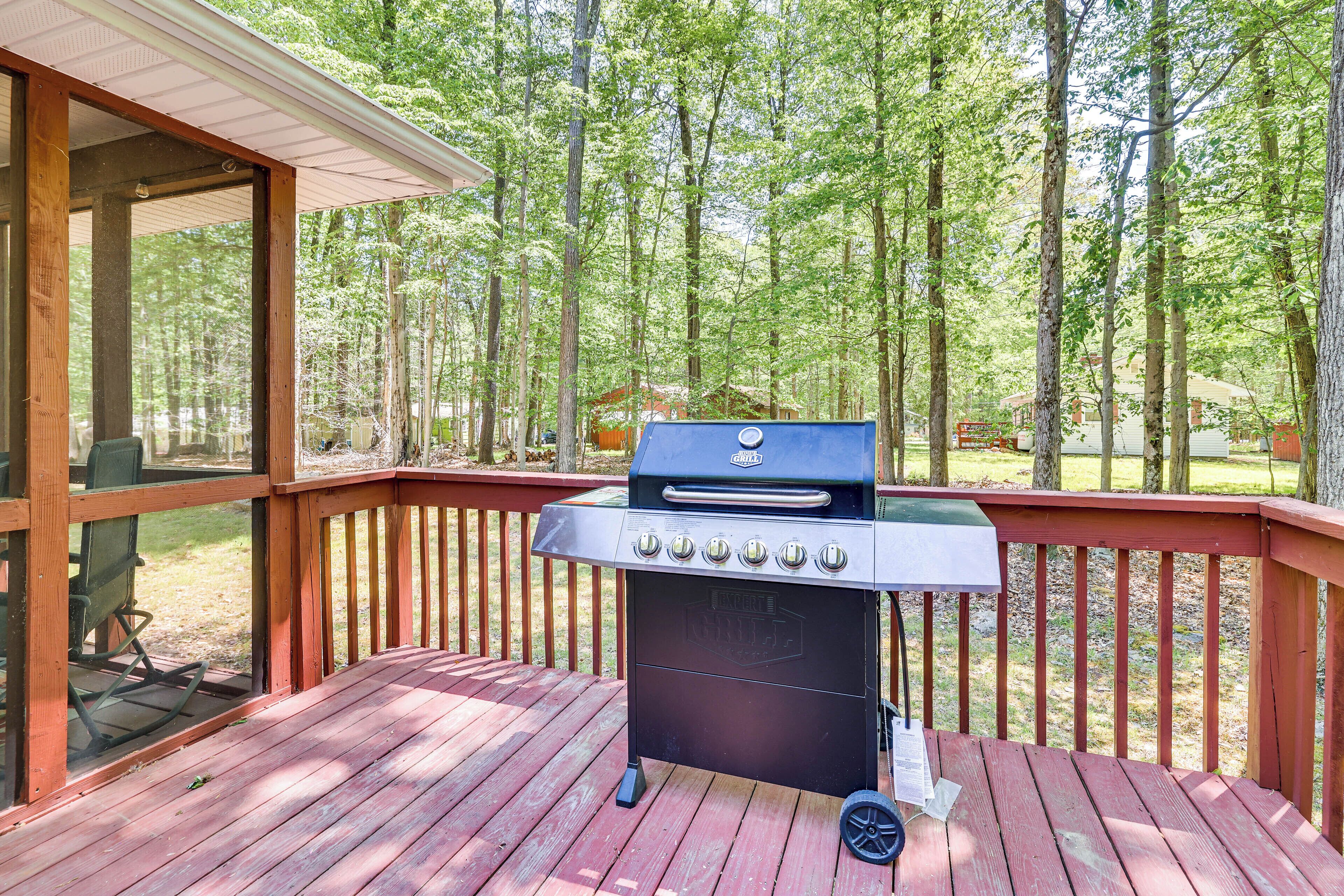A barbecue grill on a wooden deck with a view of a forest.
