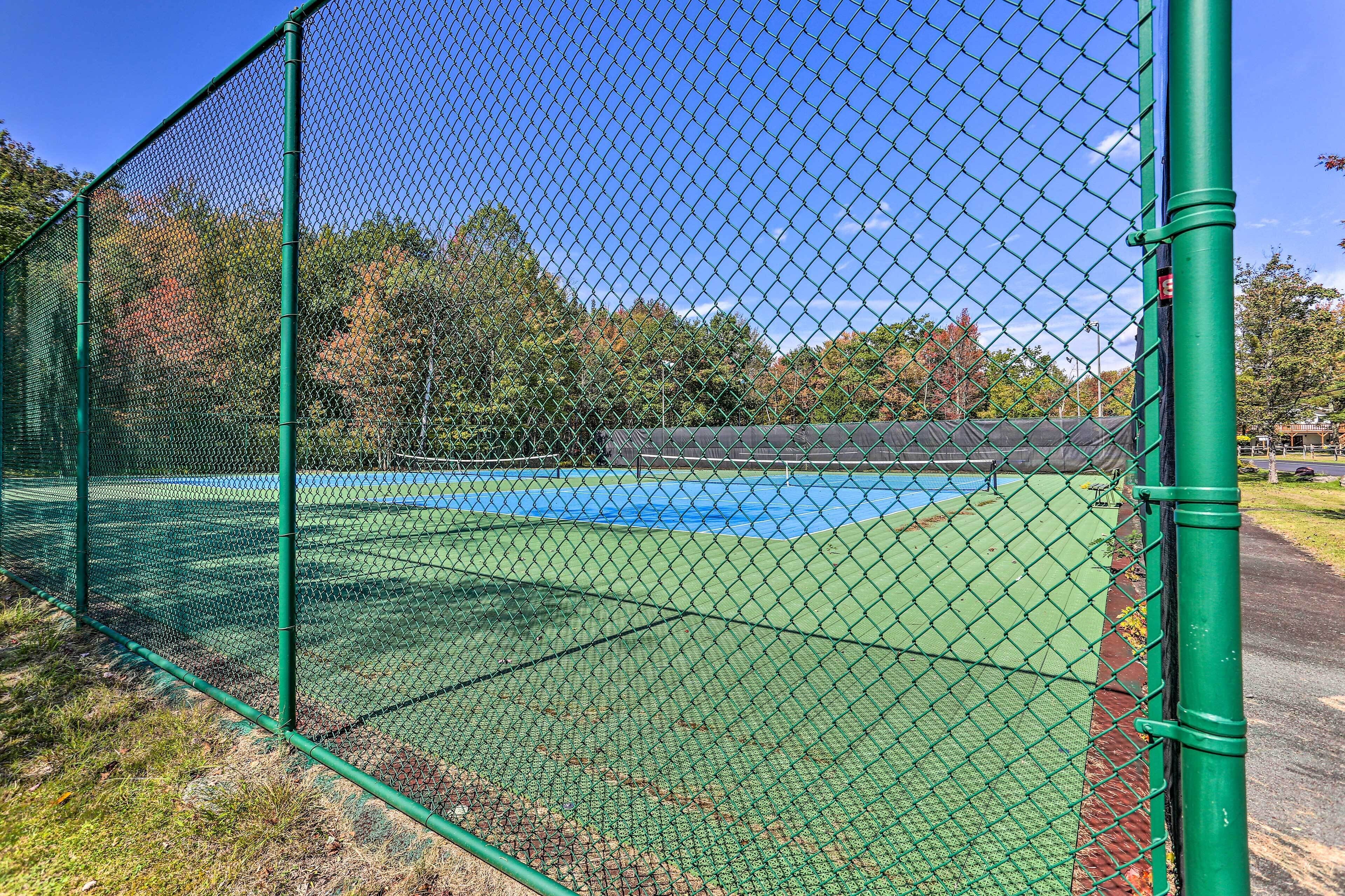 A tennis court enclosed by a green chain-link fence with trees in the background.