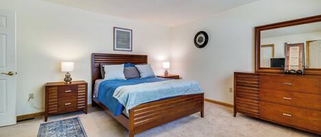 A bedroom with a wooden bed, two bedside tables, a dresser, a rug, and a wall clock.