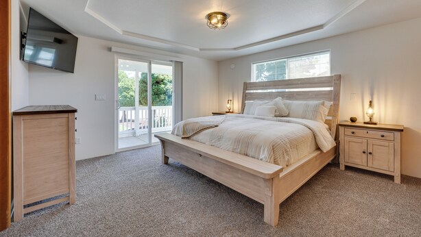 Une chambre à coucher comprenant un lit, des tables de chevet, un téléviseur fixé au mur et une porte-fenêtre coulissante donnant sur un espace extérieur.