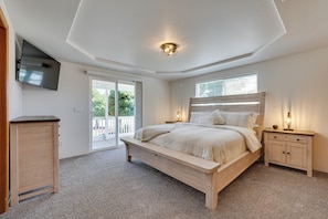 Une chambre à coucher comprenant un lit, des tables de chevet, un téléviseur fixé au mur et une porte-fenêtre coulissante donnant sur un espace extérieur.