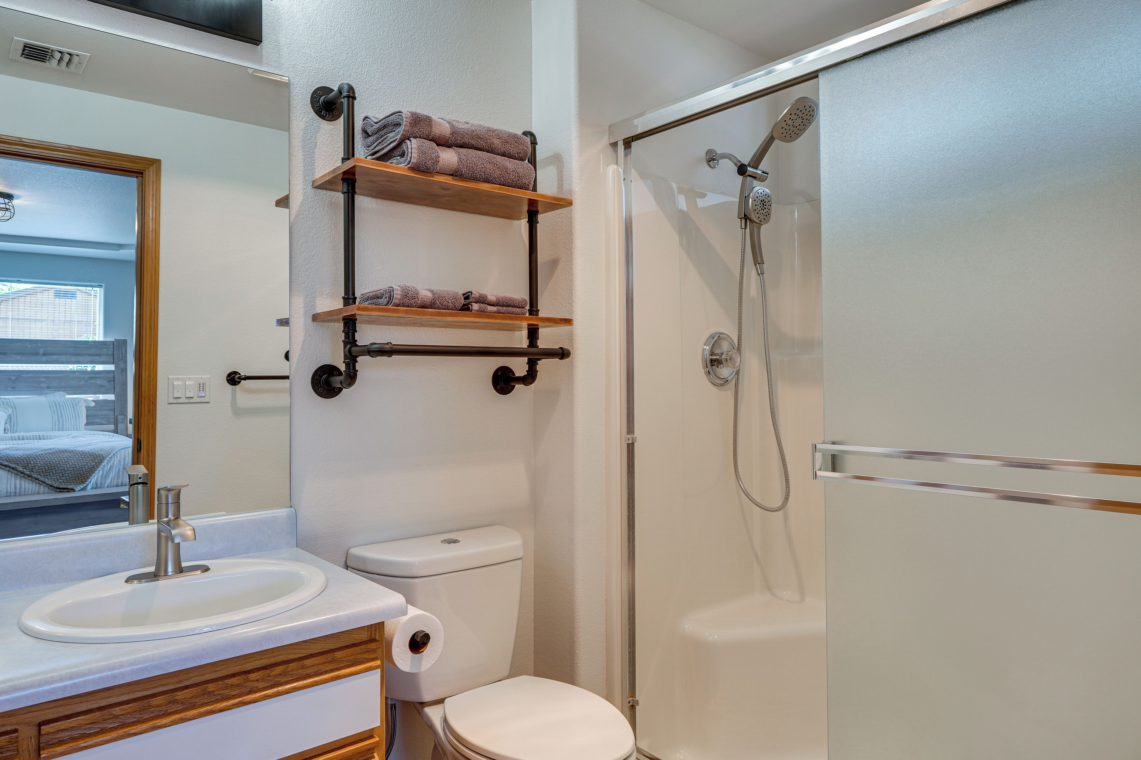 A bathroom with a sink, toilet, and shower. There are shelves with towels above the toilet.