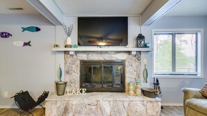 A living room with a stone fireplace, a flat-screen TV mounted above it, and decorative fish on the wall. - Waterfront Home w/ Views & Dock in Sunrise Beach! (Sunrise Beach)