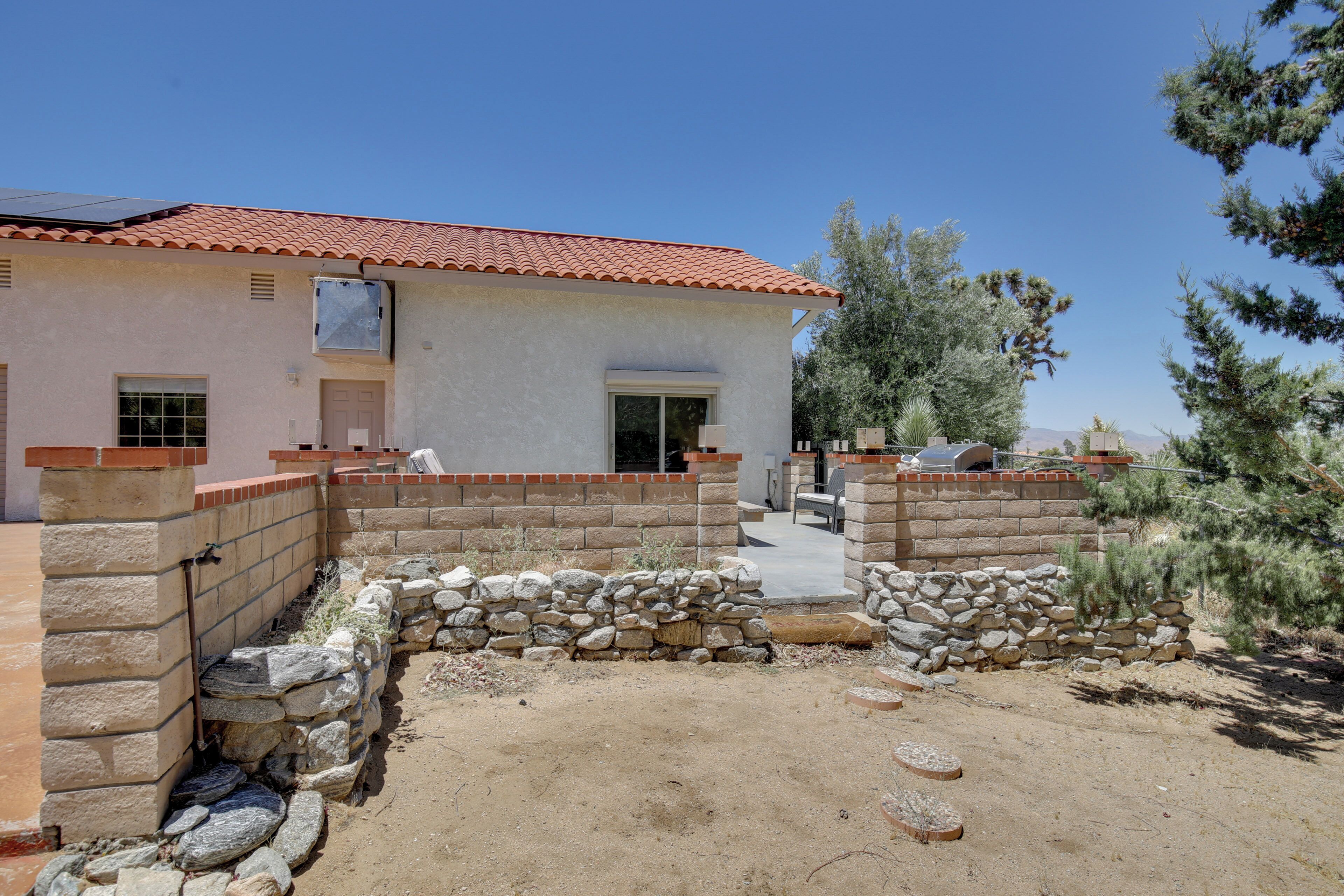 A house with a red-tiled roof, a stone wall, and a patio area with a chair and table.
