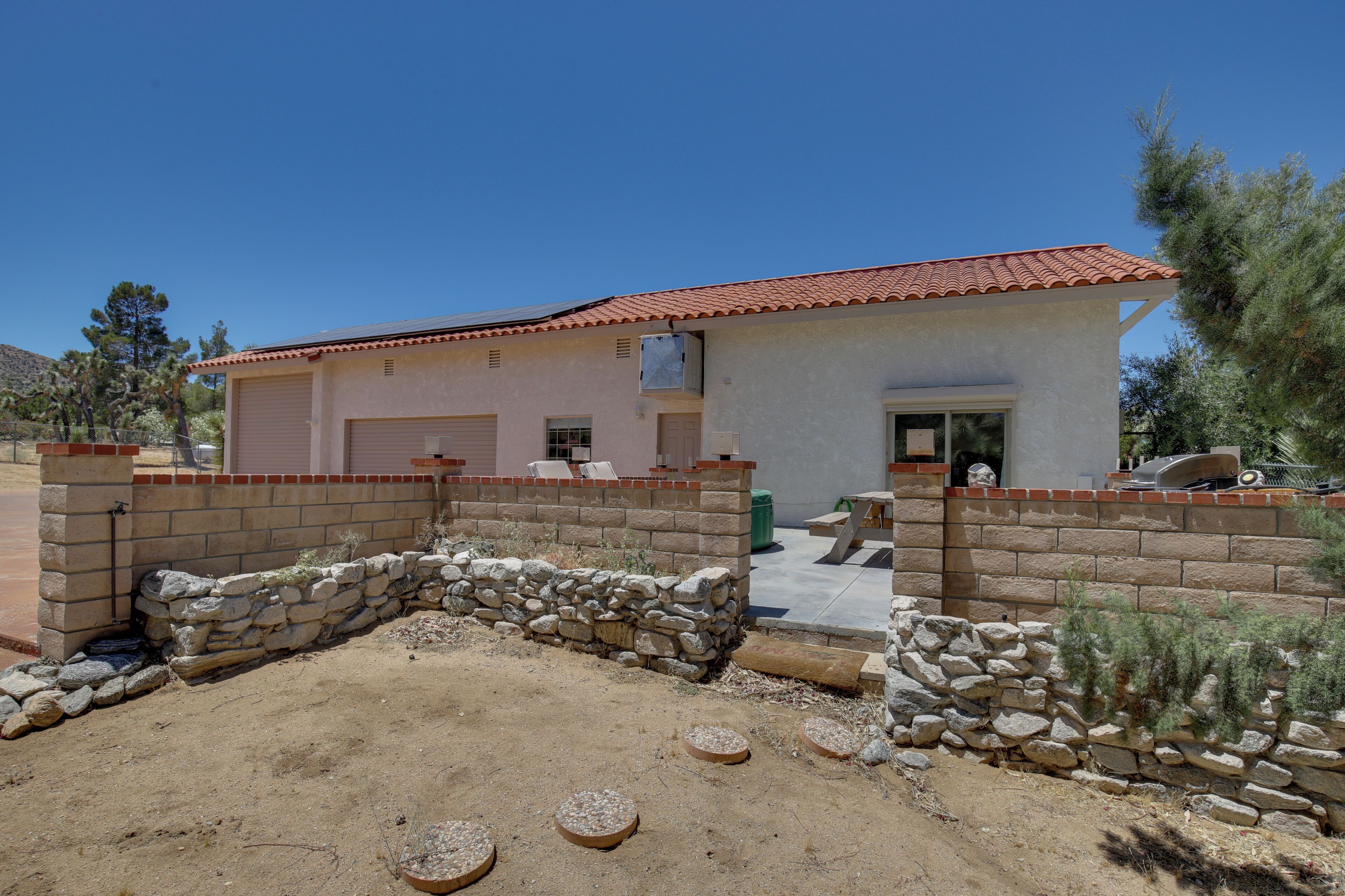 A two-story house with a red-tiled roof, a stone wall, and a patio area with a fire pit.
