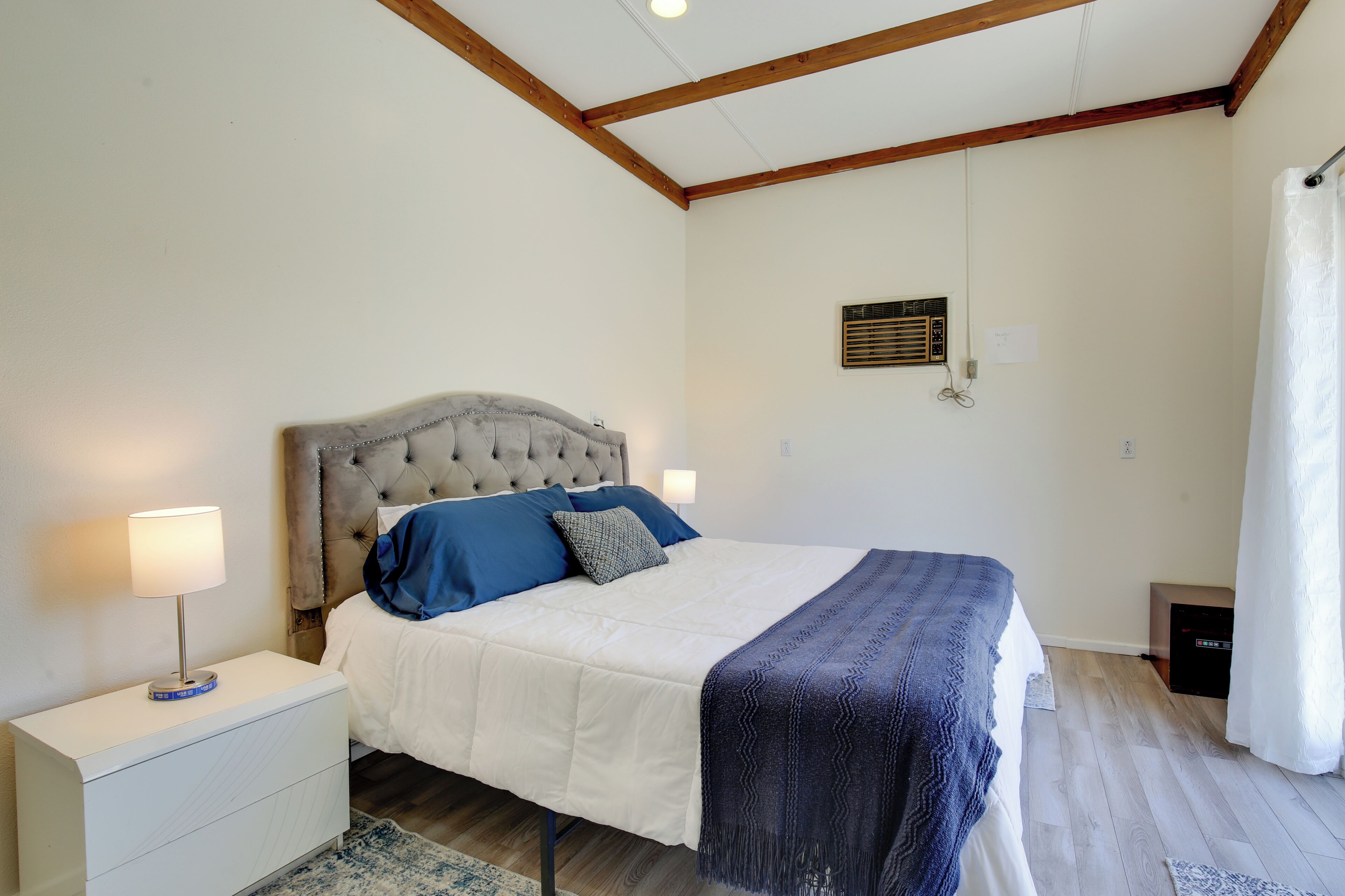 Une chambre à coucher avec un lit, des tables de chevet, une lampe, une radio et un rideau.