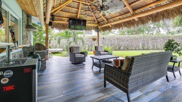 An outdoor patio with a thatched roof, wicker furniture, and a TV mounted on the ceiling.