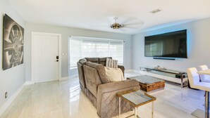 A modern living room with a sectional sofa, a glass coffee table, and a flat-screen TV mounted on the wall.