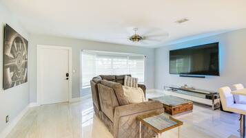 A modern living room with a sectional sofa, a glass coffee table, and a flat-screen TV mounted on the wall.