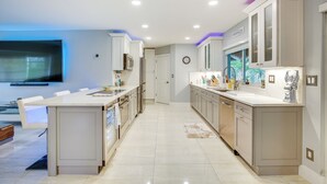 A modern kitchen with a central island, white cabinetry, and a flat-screen TV mounted on the wall.