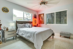 Un dormitorio con cama, mesitas de noche, un velador, un ventilador de techo, una ventana con persianas y un reloj de pared.