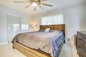 A bedroom with a bed, a ceiling fan, a nightstand, a dresser, and a window with blinds.